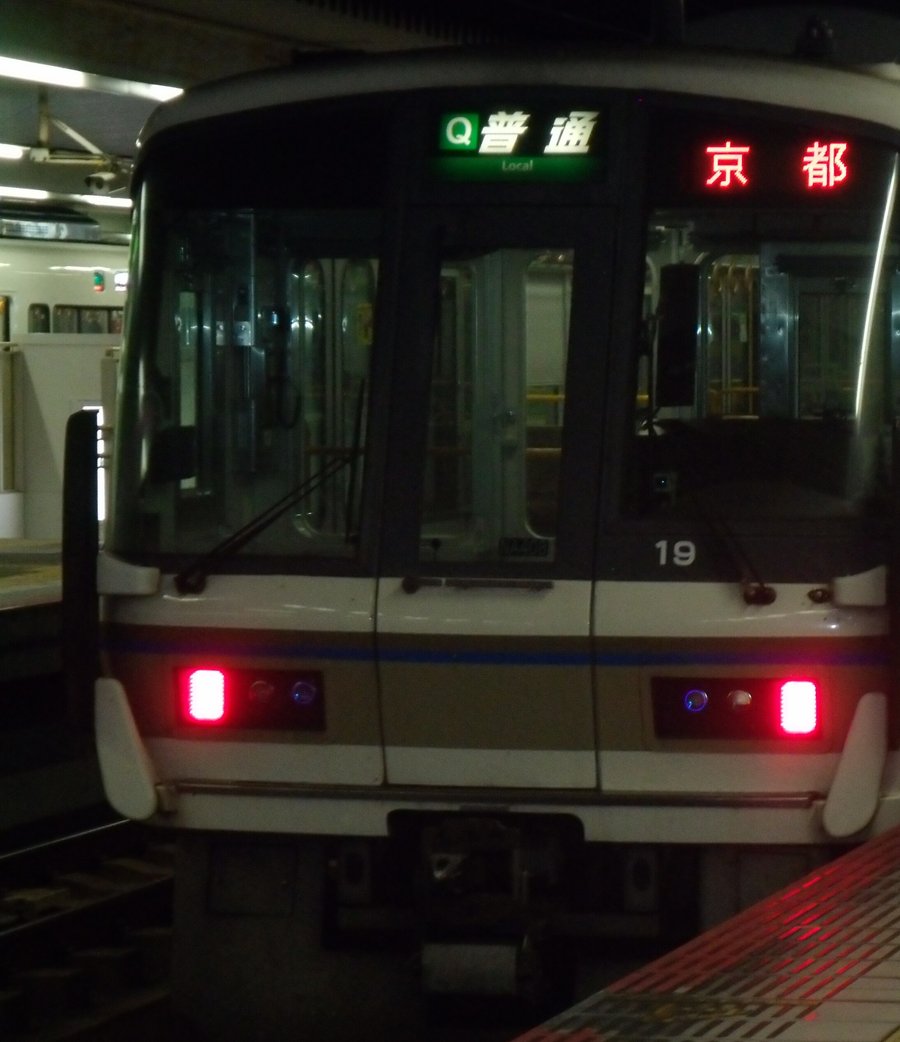 夜間奈良站月台上的 JR 西日本 221 系電車正面:車頭上方綠底看板寫「普通」,右邊紅色字幕顯示「京都」
