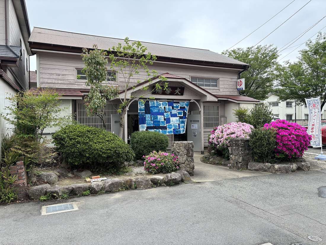 木造錢湯外觀，入口掛著藍染暖簾，屋簷側邊有「ゆ」字招牌