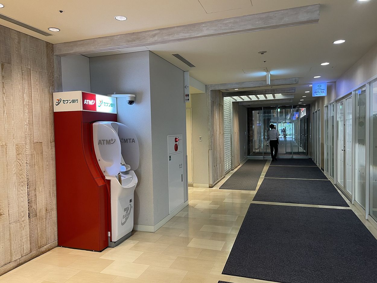 日本大樓通道內的紅色セブン銀行 ATM，機台上方有 ATM 與セブン銀行標示