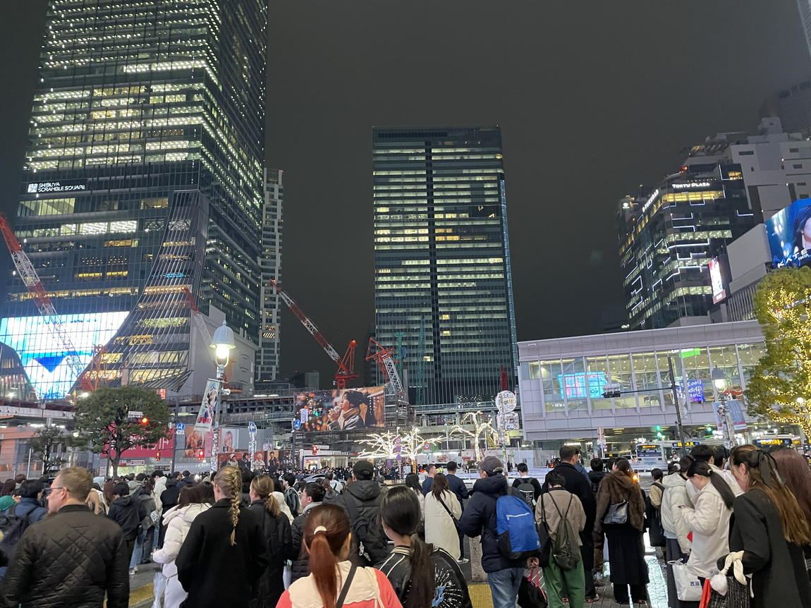 2025 年 12 月 24 日夜間的澀谷全向十字路口，人群穿著深色大衣與羽絨外套等待過馬路，背景是澀谷 Scramble Square 與澀谷站
