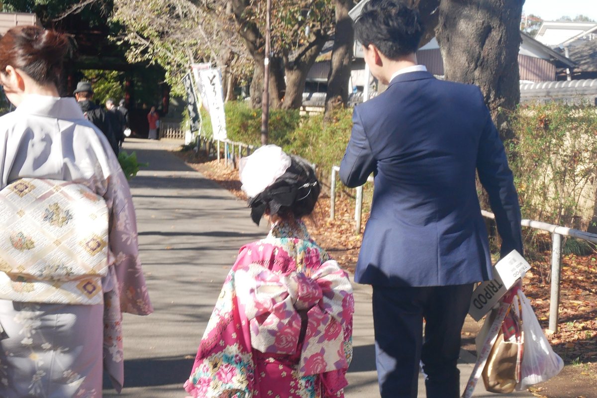 穿著七五三和服的女孩與雙親走在神社參道上,三人皆為背影