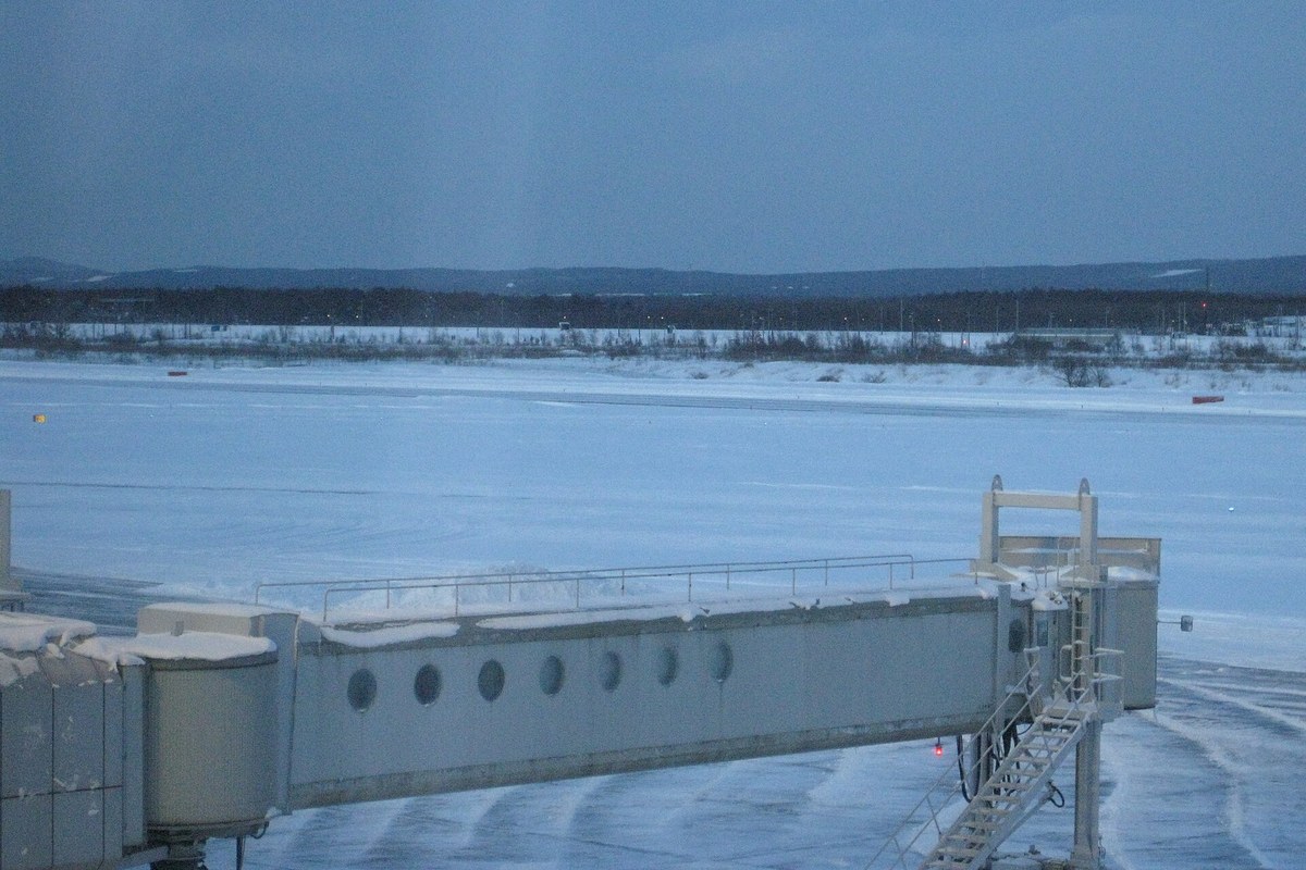 新千歲機場冬季傍晚的停機坪，空橋頂部積雪，遠方跑道與周邊草地整片被雪覆蓋
