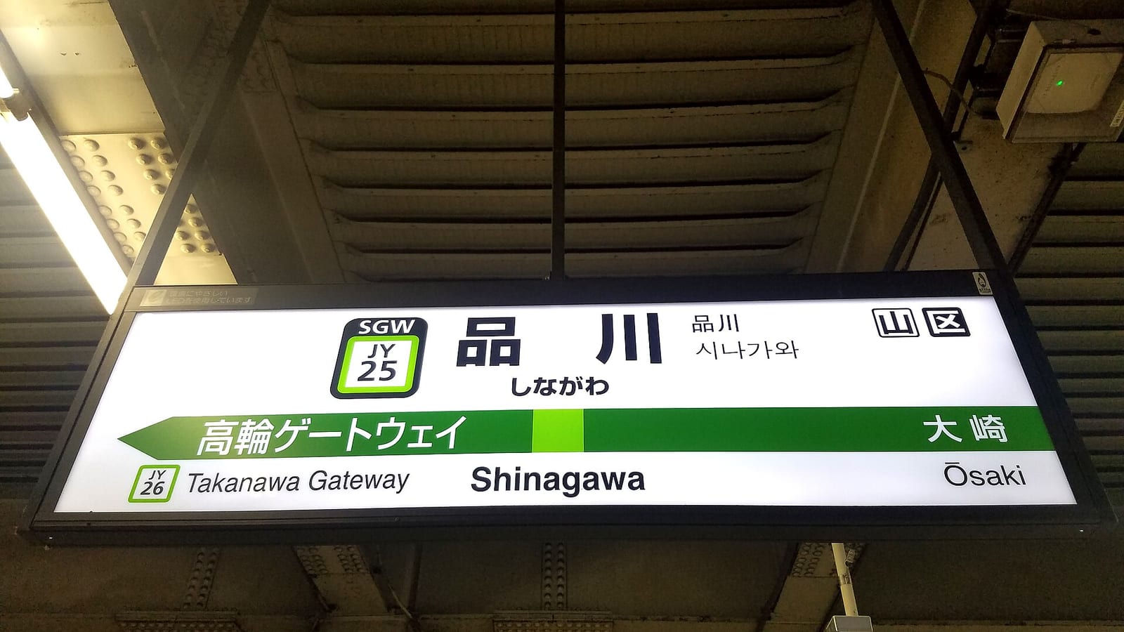 JR 品川站山手線月台懸掛的駅名標,白底黑框,中央大字「品川 しながわ Shinagawa」,左邊是綠色圓角方框的站號 JY 25,右上角另有兩個方框字「山」與「区」,下方綠色橫帶標出鄰站高輪ゲートウェイ(JY26)與大崎