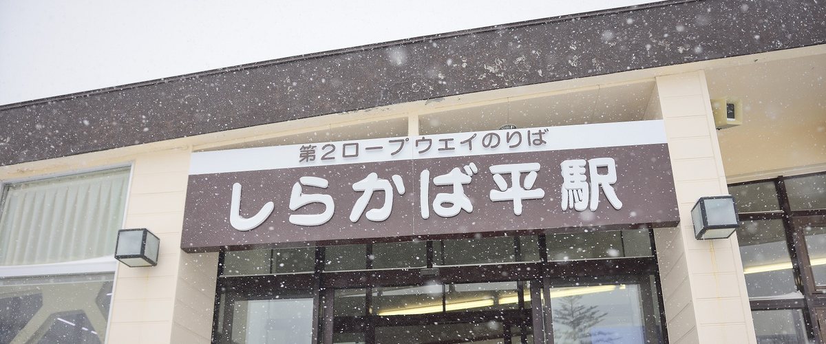 しらかば平駅的站體外觀,招牌上方小字寫「第2ロープウェイのりば」,畫面裡正在下大雪