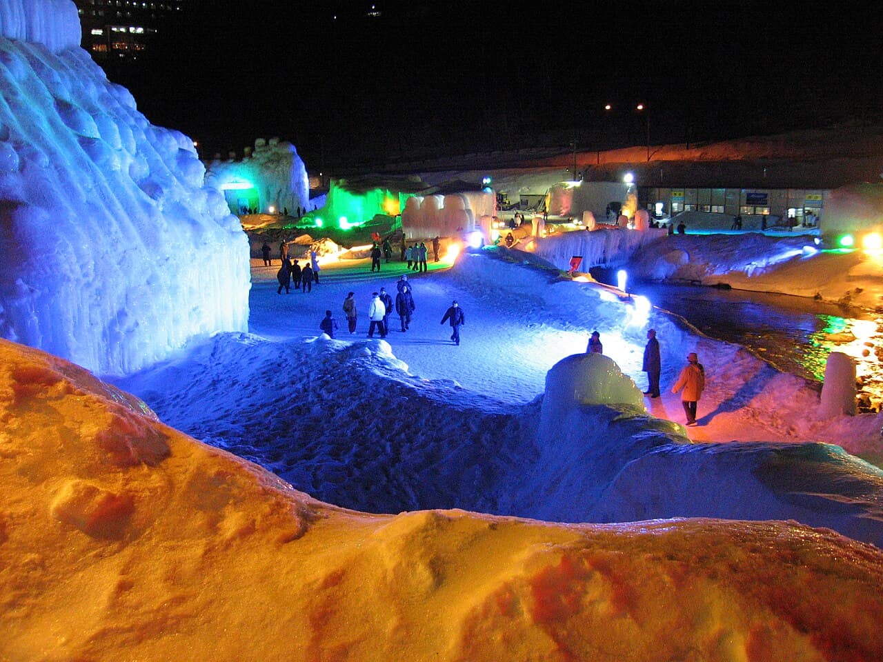 層雲峽冰瀑祭夜間會場,藍色與橘色燈光打在冰塔與雪道上,遊客走在其間