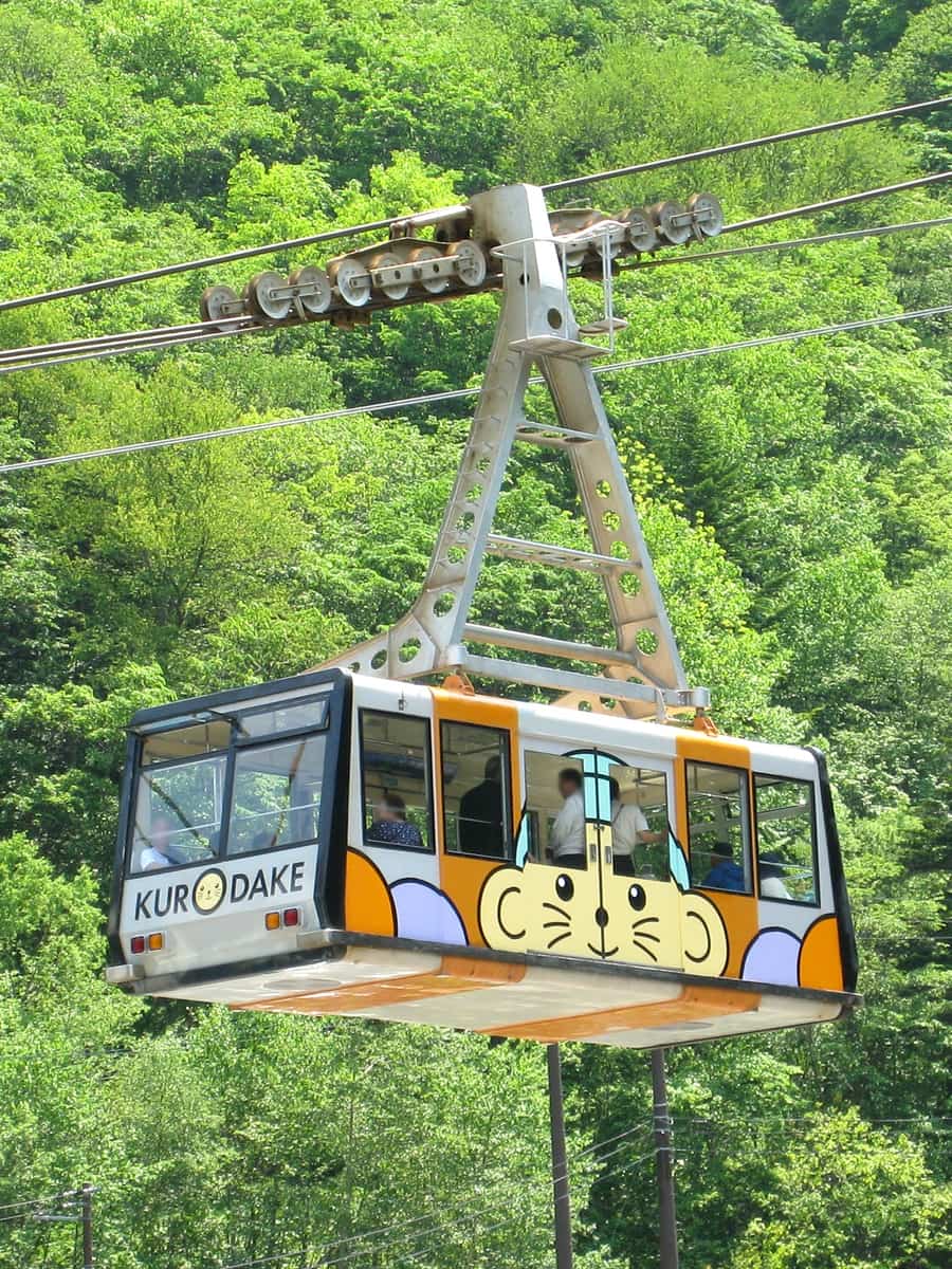 黑岳纜車車廂行駛在新綠森林上方,車身漆著 KURODAKE 字樣與吉祥物圖案