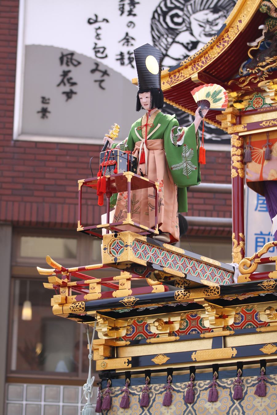 高山祭三番叟屋台的からくり人形,身著綠色狩衣、手持扇子立於屋台前方的橋樑機構上