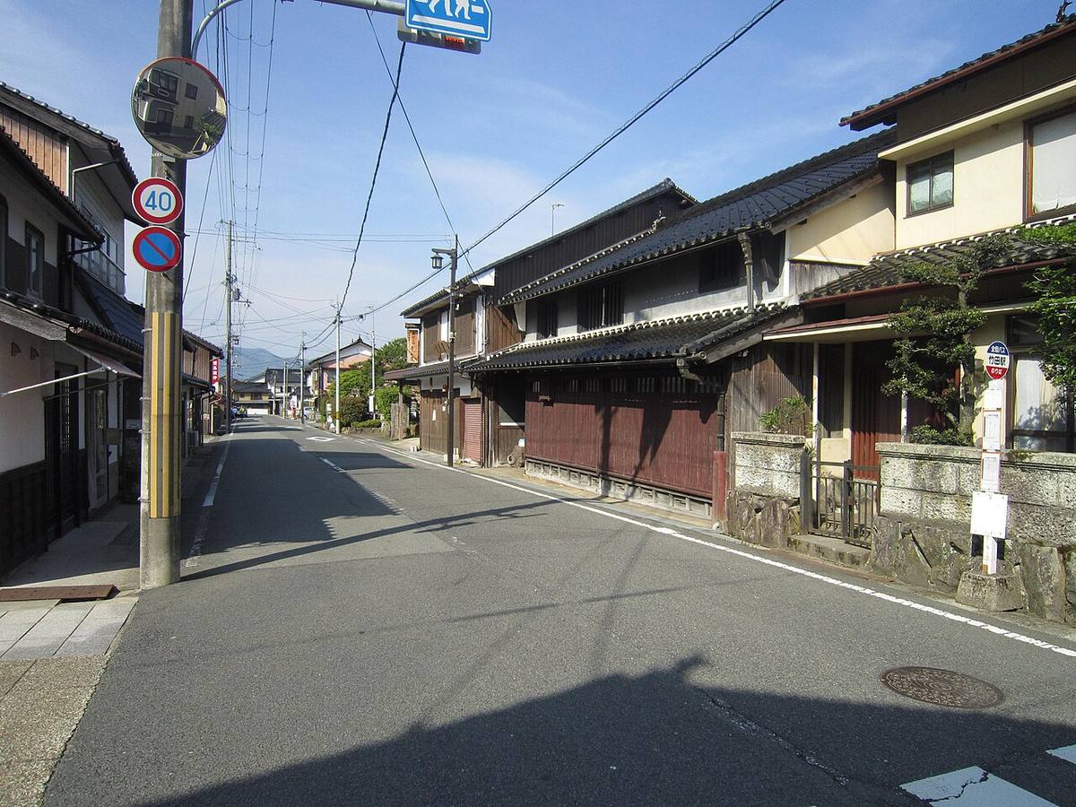 竹田城下町的街道:一側是深色木造格子門面的傳統町屋與石砌矮牆,路旁立著巴士站牌與速限 40 標誌,街道盡頭望得到山稜