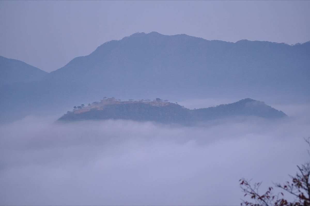破曉時分從立雲峡望向竹田城跡:城跡所在的山稜浮在一片白色雲海之上,山頂隱約看得到石垣的線條,遠方是層疊的山影