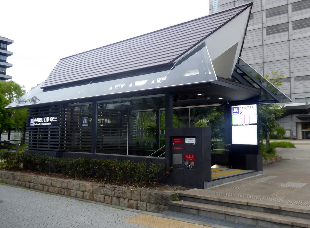 谷町四丁目站 9 號出入口：黑色格柵牆加斜屋頂的地面出入口建築，牆上有 Osaka Metro 標誌和「谷町四丁目駅」站名，右側是往下的樓梯