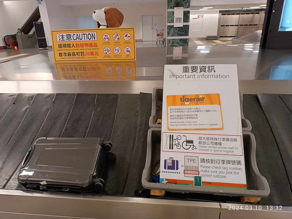 桃園機場行李轉盤上的黃色檢疫警示牌,寫著違規攜入動植物產品首次最高可罰 20 萬元,後方立著檢疫米格魯立牌
