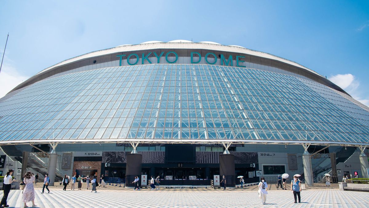 東京巨蛋外觀:白色膜構造屋頂在藍天下呈現圓弧形,外牆環繞著看板與入場口,前方廣場有行人與樹木