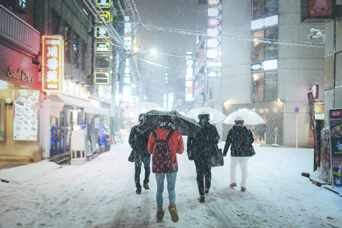 2018 年 1 月 22 日降雪中的新宿歌舞伎町街頭,行人撐傘走在已被雪覆蓋的路面上,兩側霓虹招牌仍亮著
