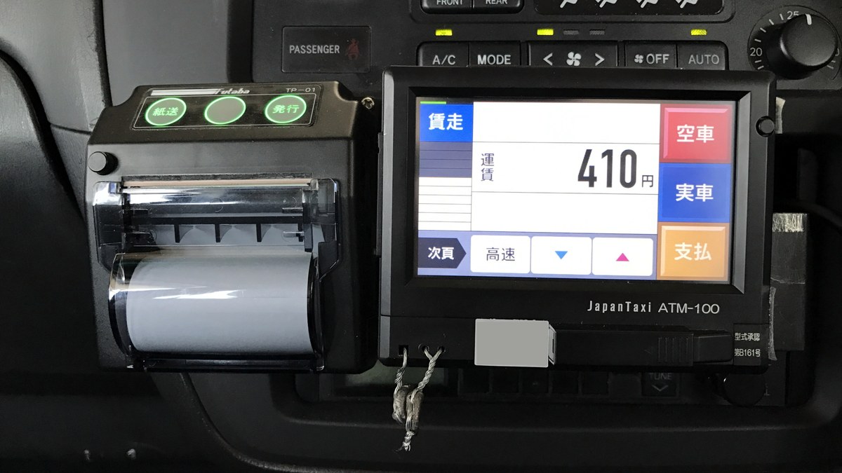 日本計程車車內的 JapanTaxi ATM-100 跳表機與收據列印機,畫面顯示「運賃 410 円」以及空車・實車・支払按鍵