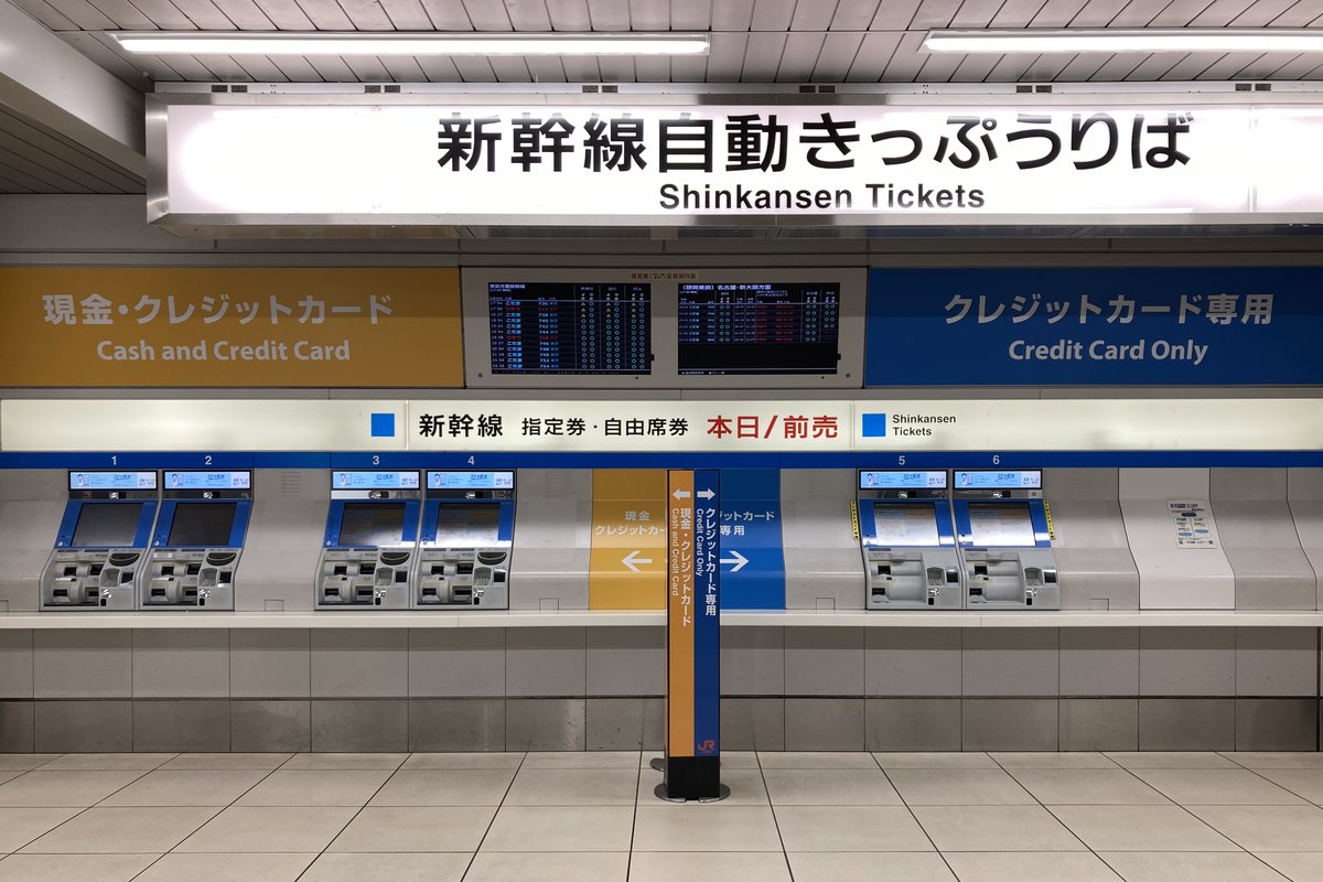 日本車站內一整排六台新幹線自動售票機,上方燈箱寫著「新幹線自動きっぷうりば / Shinkansen Tickets」,機台上方的橫幅寫著「新幹線 指定券・自由席券 本日/前売」,左半區標示現金・クレジットカード、右半區標示クレジットカード専用,中央掛著兩面發車時刻顯示板