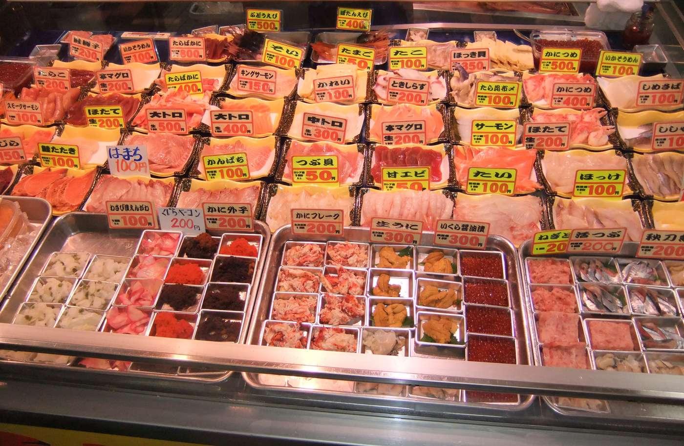 釧路和商市場店頭的勝手丼配料櫃,各式生魚片與海膽鮭魚卵標著單價