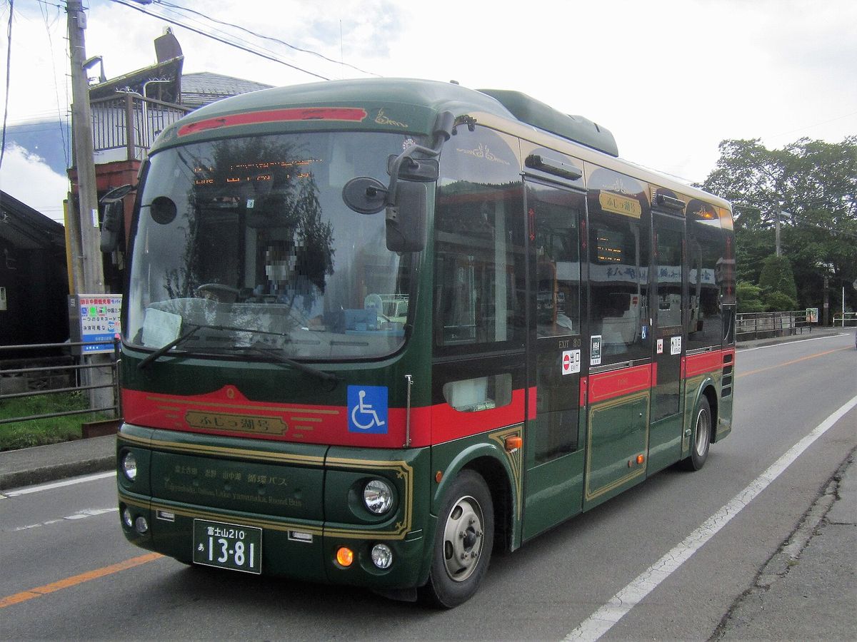 墨綠車身配紅色腰線的小型巴士開在路上,車頭和車側的金框牌子寫「ふじっ湖号」,車頭下方寫「富士吉田 忍野 山中湖 循環バス」,駕駛的臉已打馬賽克