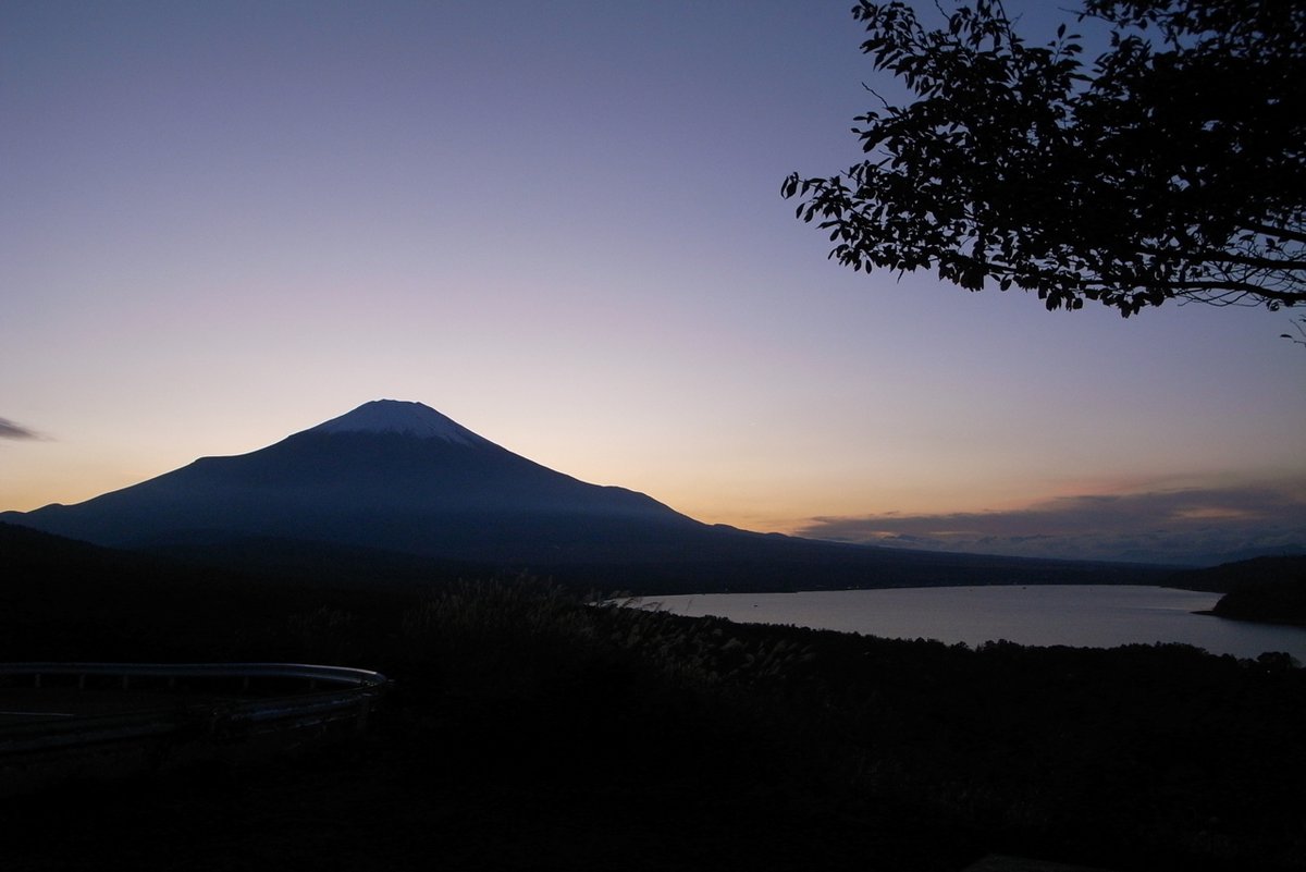 日落後從パノラマ台看山中湖:富士山成了深色剪影,地平線上一道橘色晚霞往上漸層成淡紫色天空,右下是暗下來的湖面,右上角有樹枝剪影