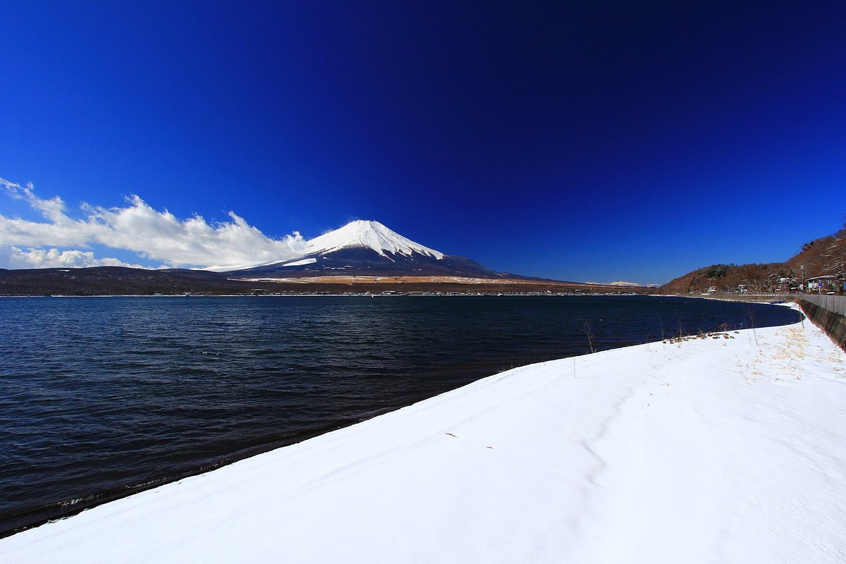 2 月的山中湖北岸:湖邊沙灘整片被白雪蓋住,雪面延伸到水邊,湖對岸是雪頂富士山,天空深藍