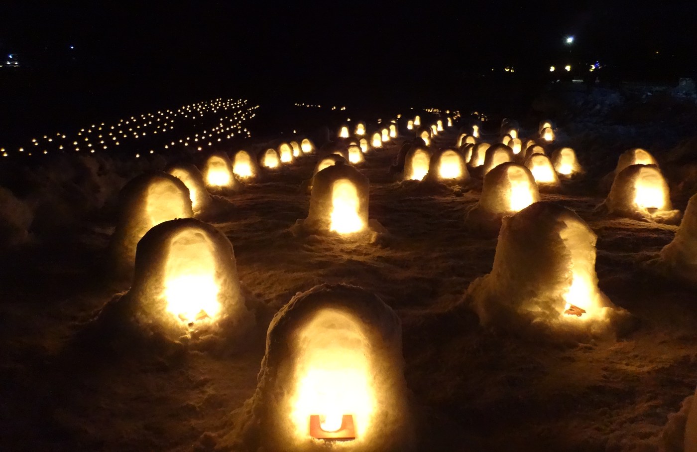 湯西川溫泉かまくら祭的夜晚,雪地上一排排點著燭火的小雪屋,遠方還有成排的燈火延伸進黑暗