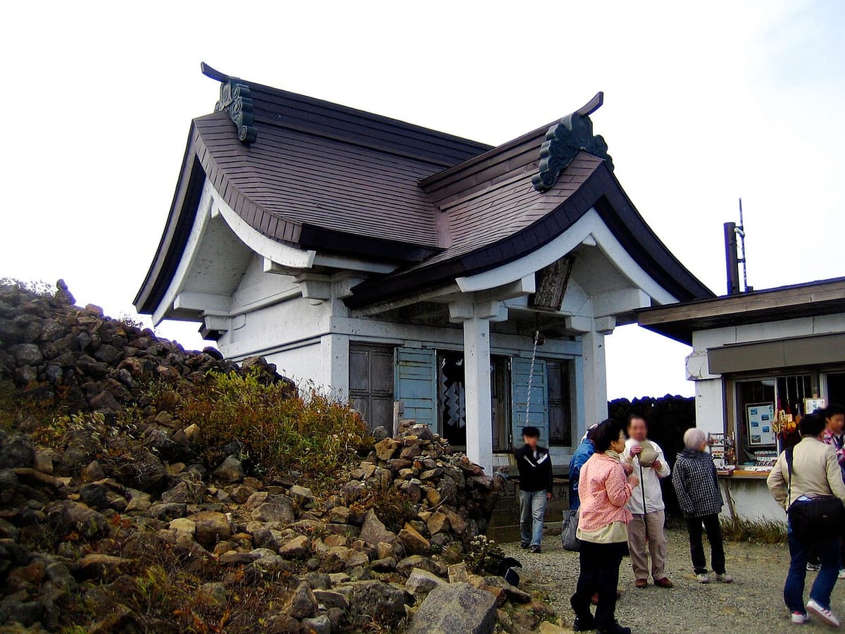 刈田岳山頂的刈田嶺神社奧宮社殿，白牆社殿旁堆著火山岩，參拜者聚在殿前